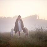 Frau läuft mit Hunden in nebliger Morgenstimmung