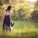 Frau mit Hund auf einer Wiese im Abendlicht