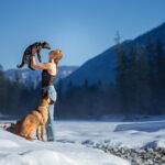 Frau mit zwei Hunden beim Fotoshooting in winterlicher Berglandschaft